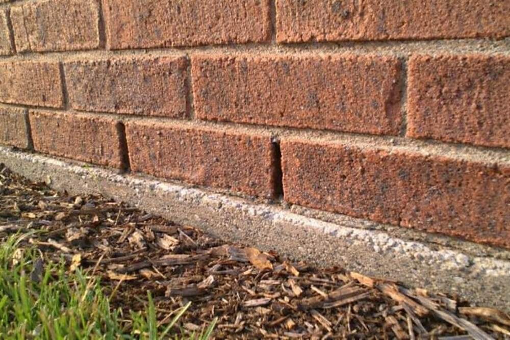The base course of a brick veneer wall with open weep holes between the bricks