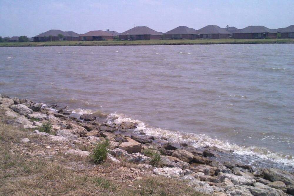 The shoreline of a reservoir with houses beyond