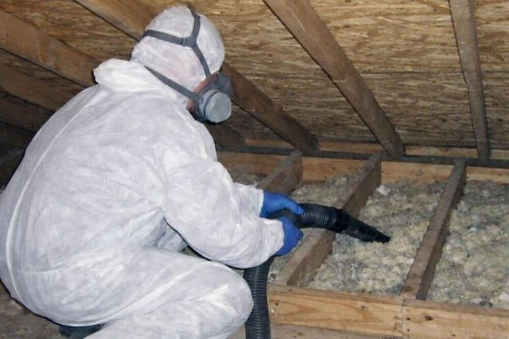 A person in a white protective suit and respirator, face out of frame